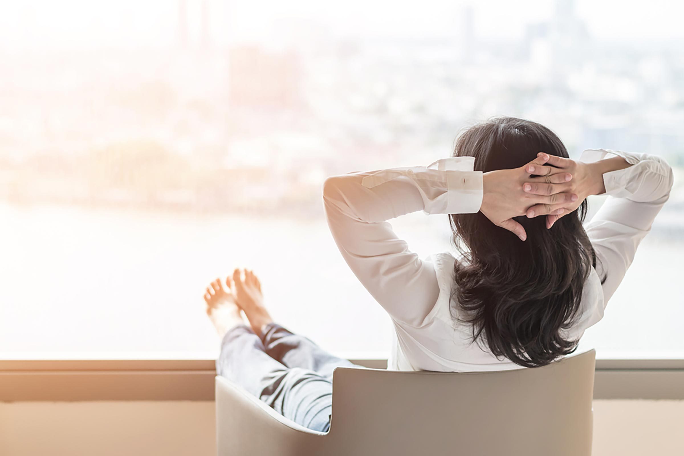 woman relaxing with hands behind head and looking out window