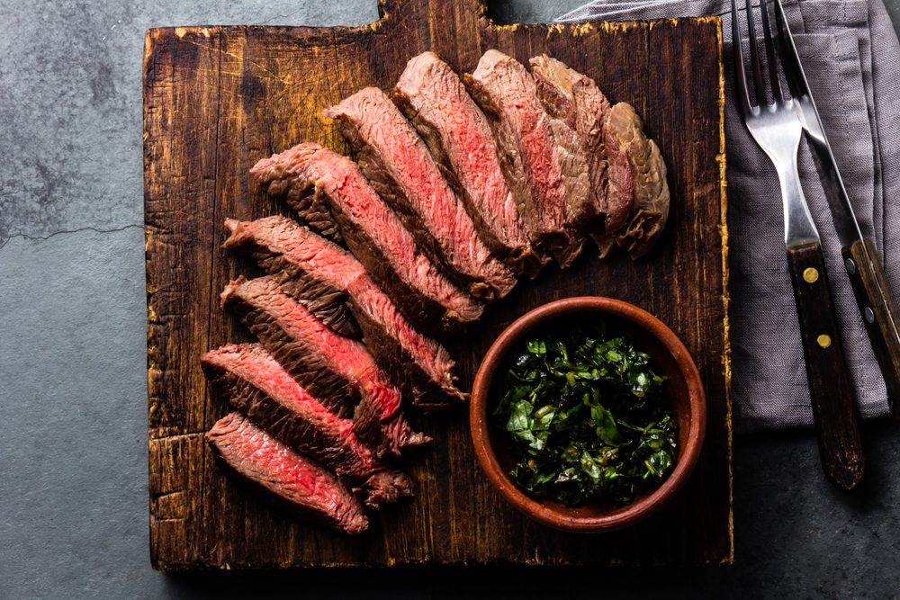 Medium rare sliced beef served on wooden board. Sliced medium rare roast beef on slate gray background