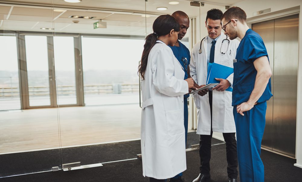 Diverse multiracial medical team consulting on a patient records standing in a foyer at a hospital grouped around a tablet computer
