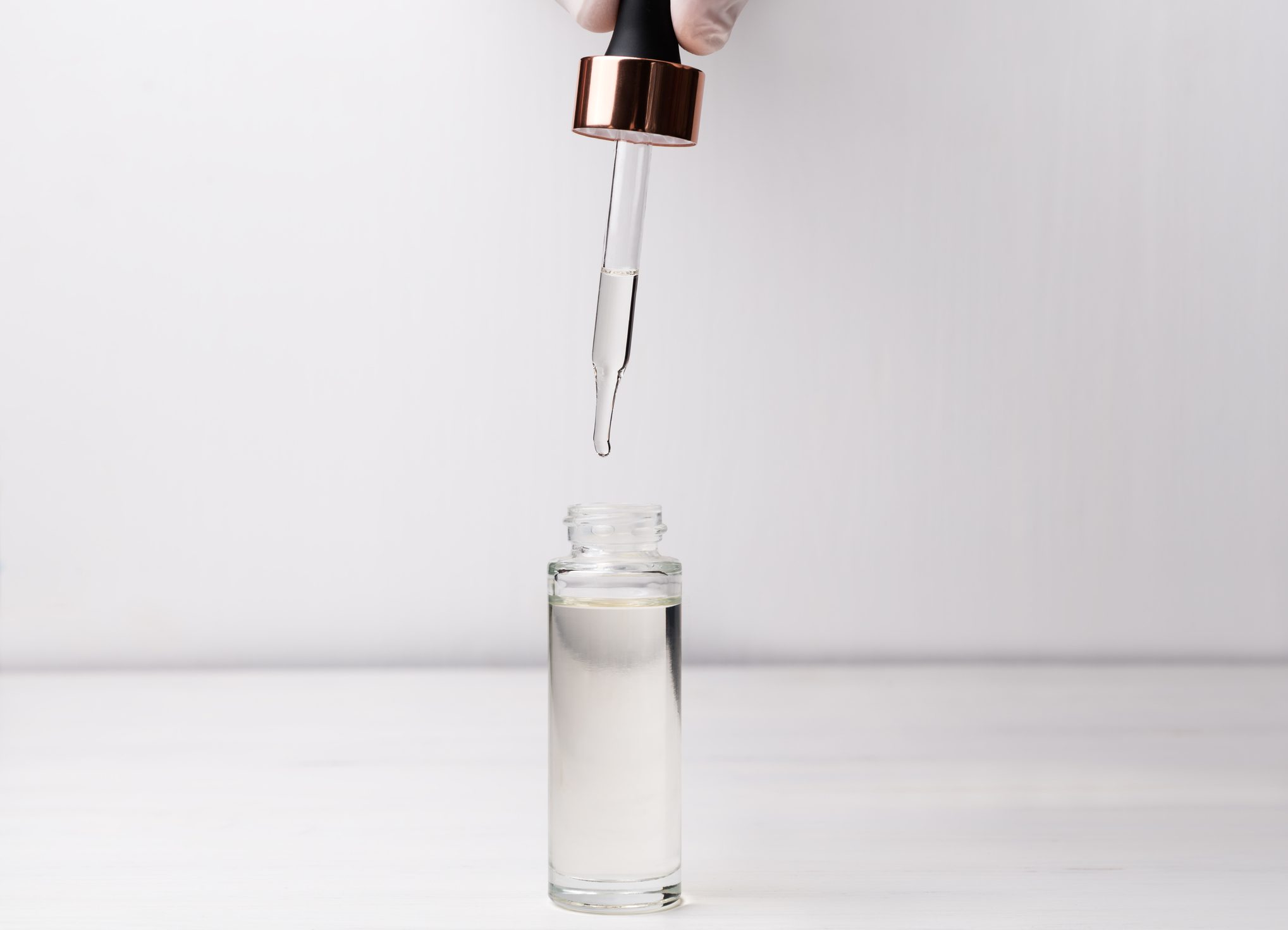 Hand in medical gloves holding dropper and bottle of beauty serum. Beauty product for skincare concept.