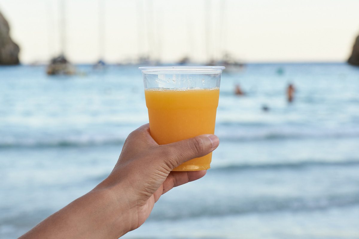 hand holding a glass of orange juice with a cove full of boats in the background